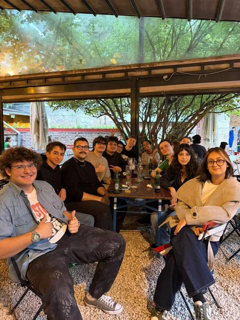 A long table of students in the garden at The Grund, under the trees, giving the camera a thumbs up
