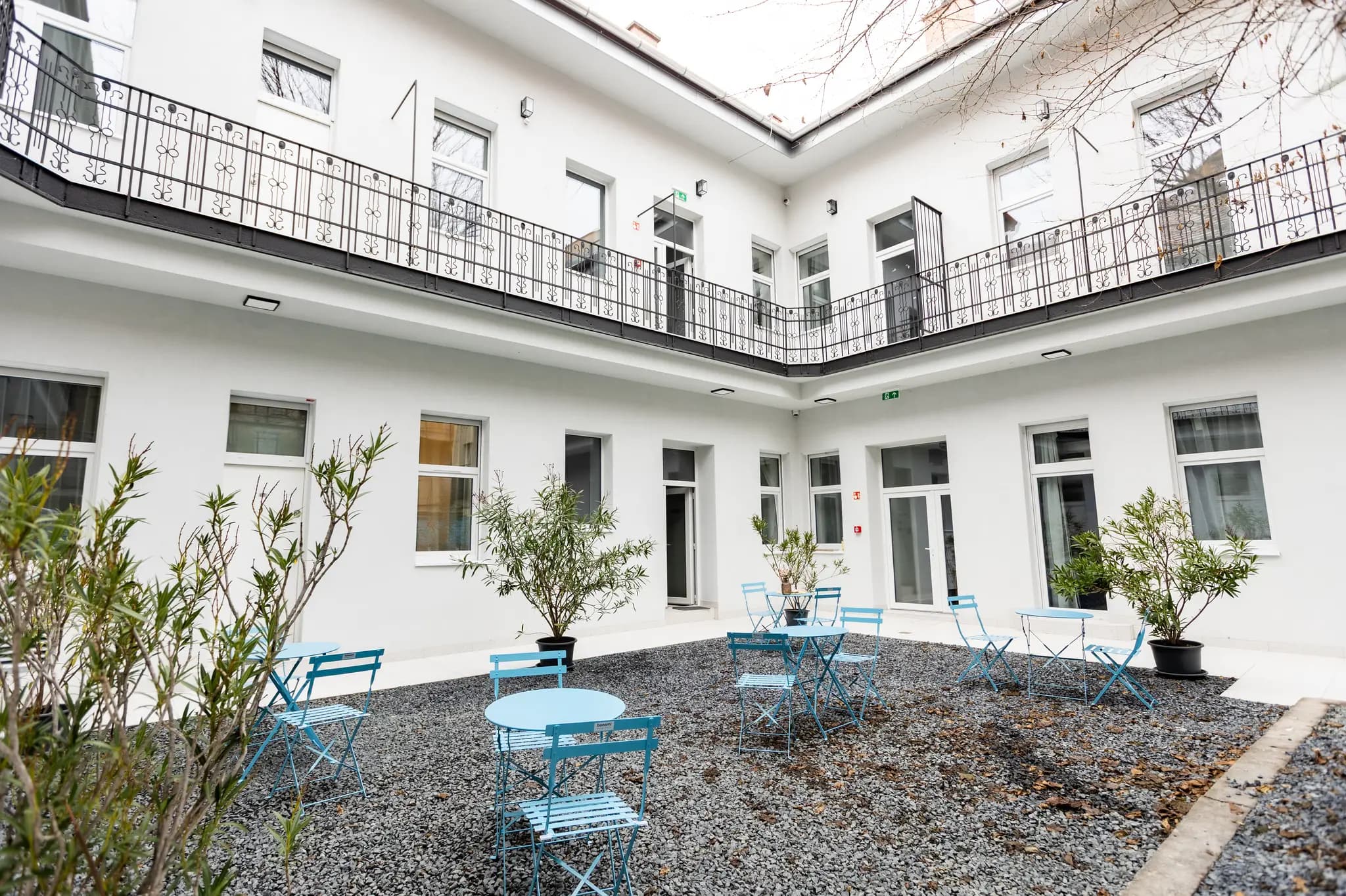 The inner courtyard garden of Gát utca 19, Budapest, with blue bistro tables and potted plants